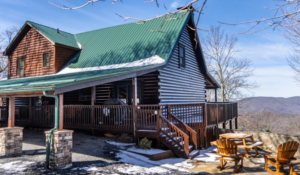 a beautiful cabin for sale in Boone NC, with light snow on the ground and the roof and mountains are in the background